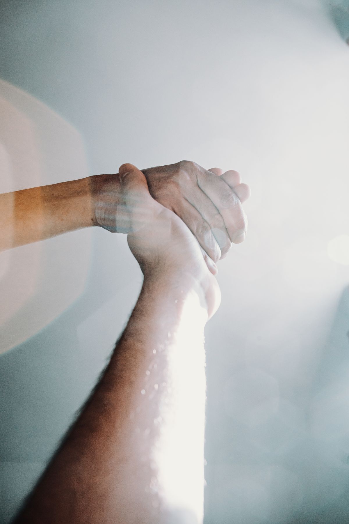 Two hands clasped together in a supportive grip, bathed in warm light — love and kindness